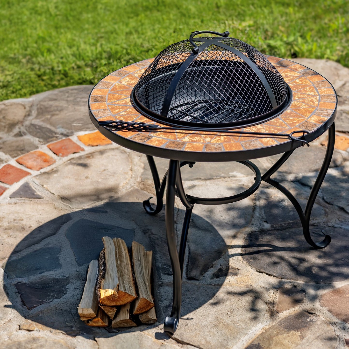 Round stone fire pit table with black metal mesh cover and firewood on a stone patio.