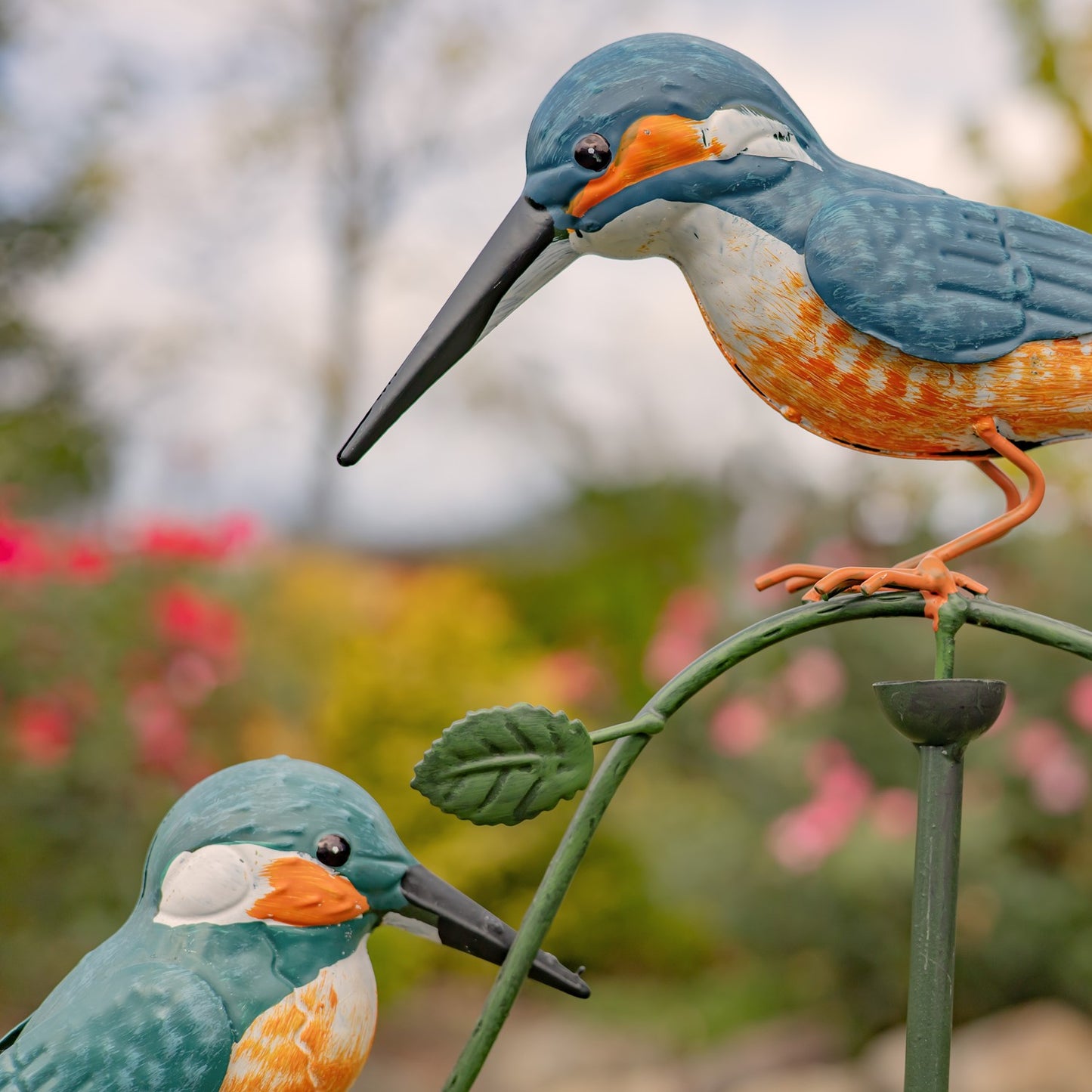 Two decorative kingfisher bird figures on a branch with a blurred floral background