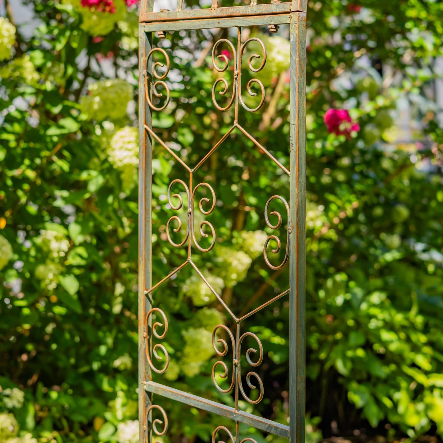 Decorative metal trellis with intricate patterns against a blurred garden background