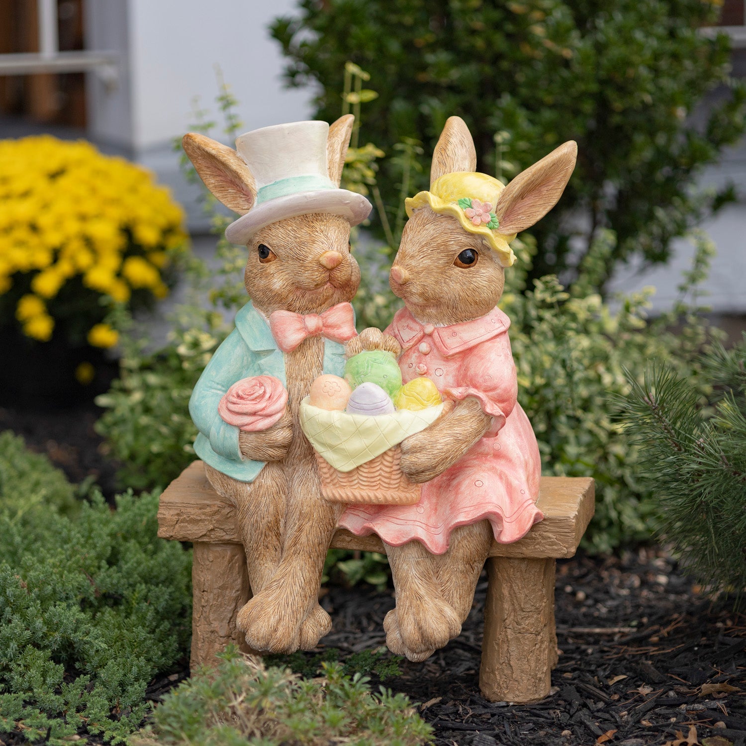 Easter bunny garden statues sitting on a bench holding a basket of eggs