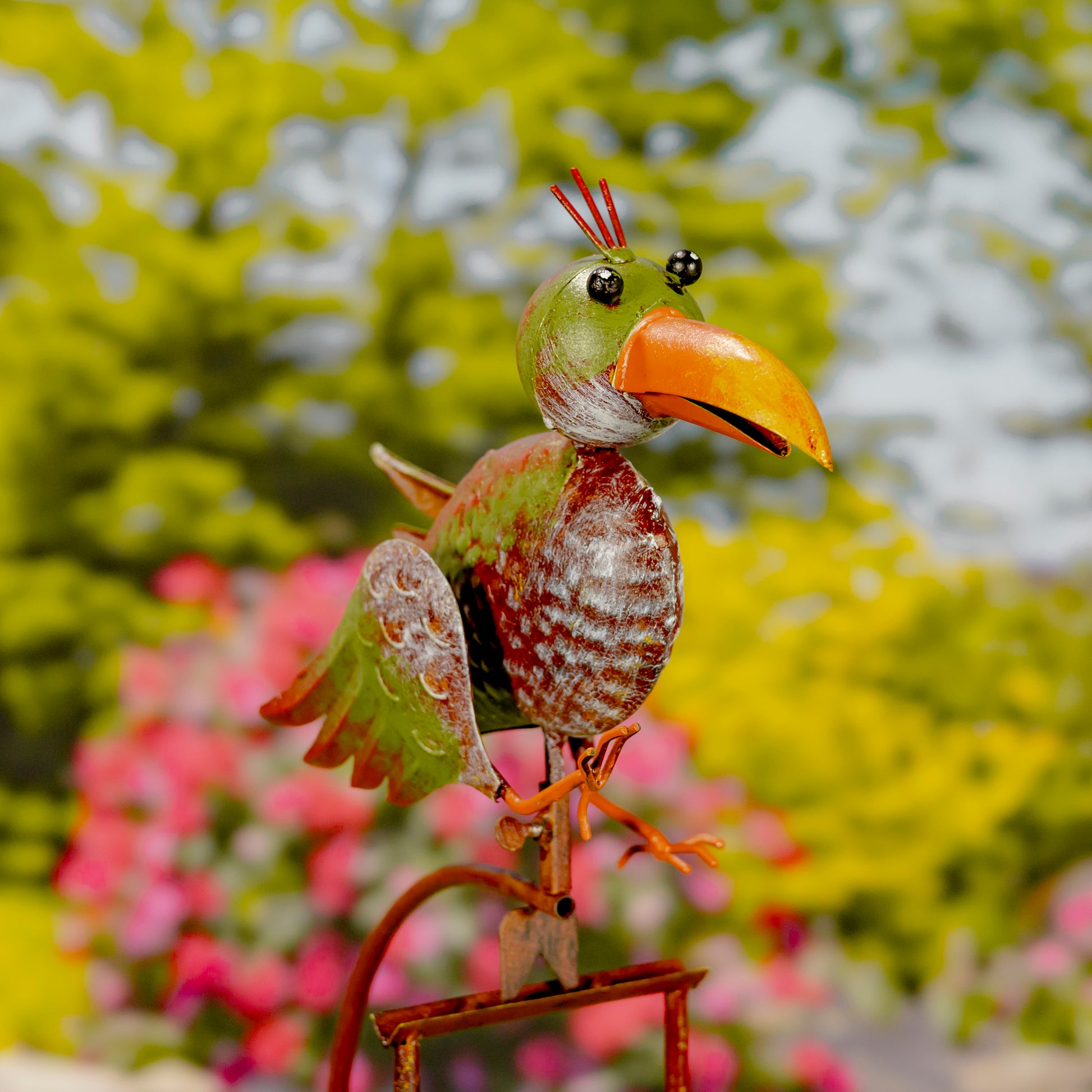 Decorative metal bird sculpture with a colorful beak against a blurred garden background