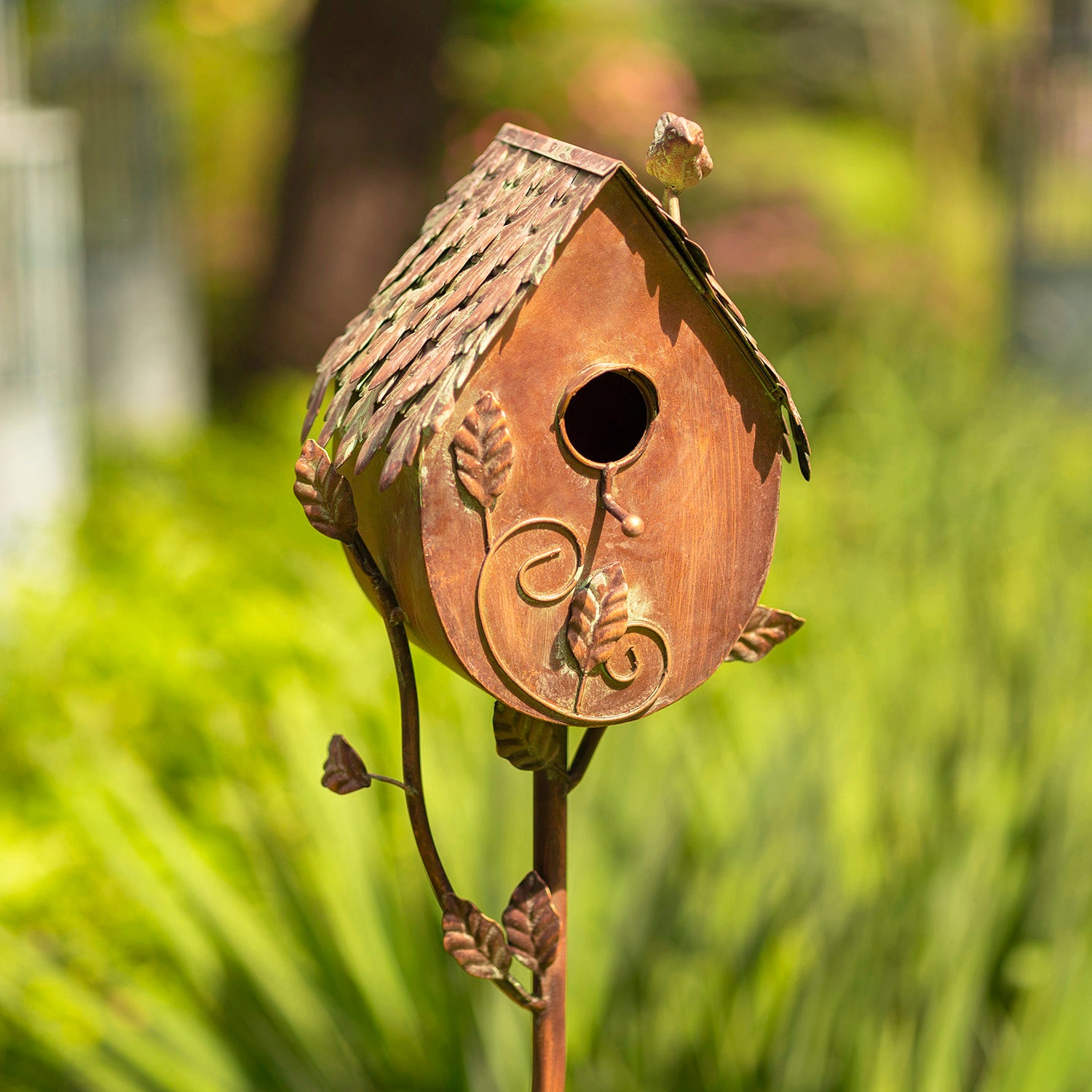 Decorative birdhouse on a stand with a blurred green garden background