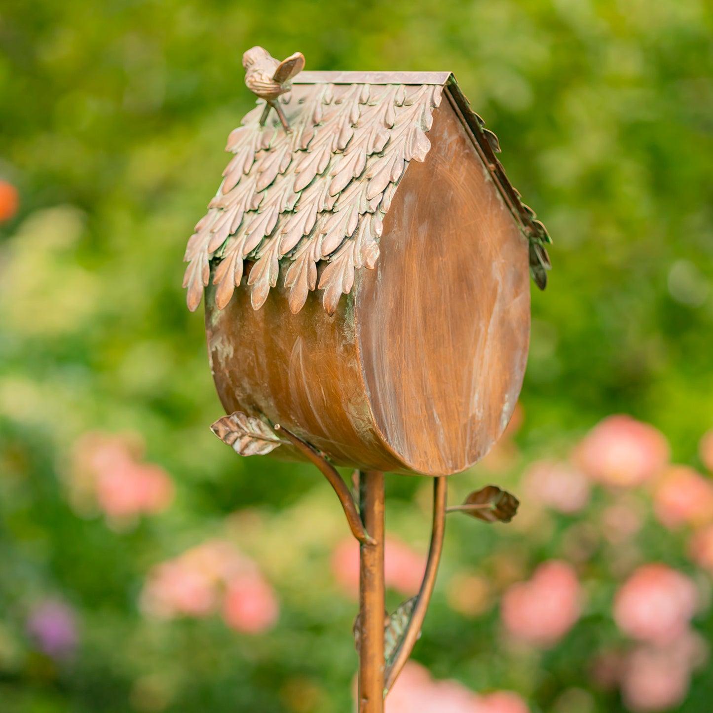 Decorative birdhouse shaped like a brown acorn with a small bird on top, set against a blurred garden background.