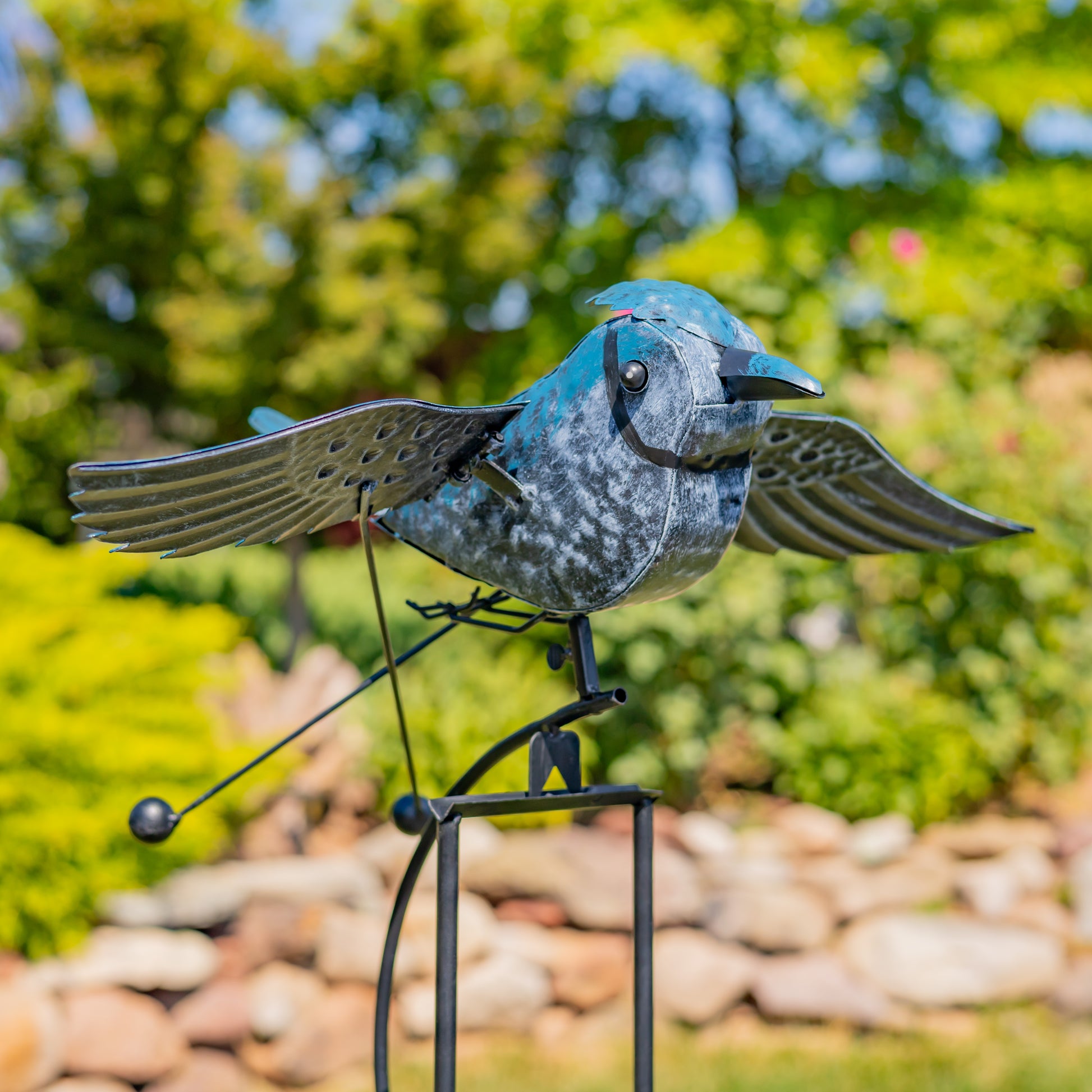 Decorative metal bird sculpture in a garden setting with blurred greenery in the background