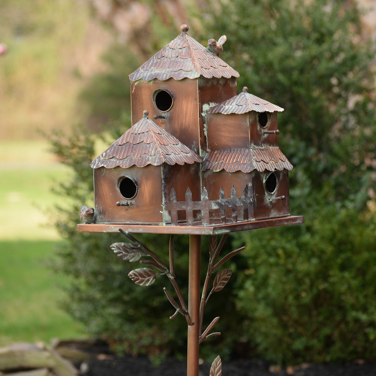 Decorative copper birdhouse sculpture with multiple compartments on a stand outdoors.