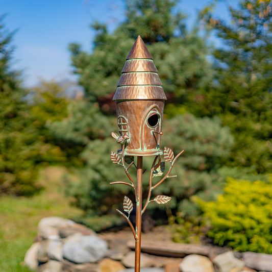 Decorative birdhouse on a stand with a natural background of trees and rocks.