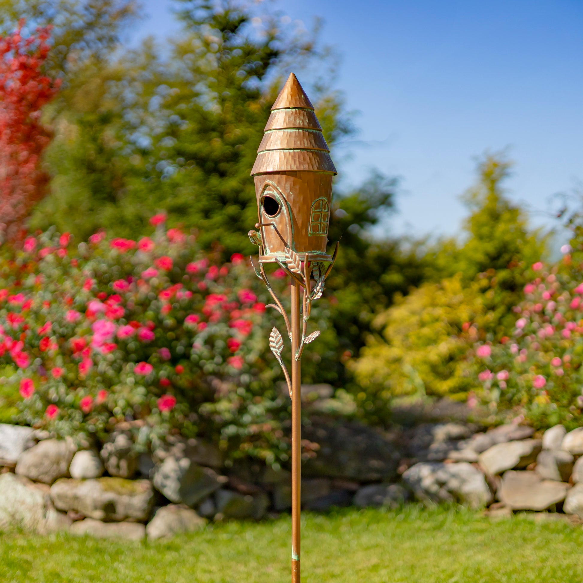 Decorative birdhouse on a garden stake with flowers and rocks in the background