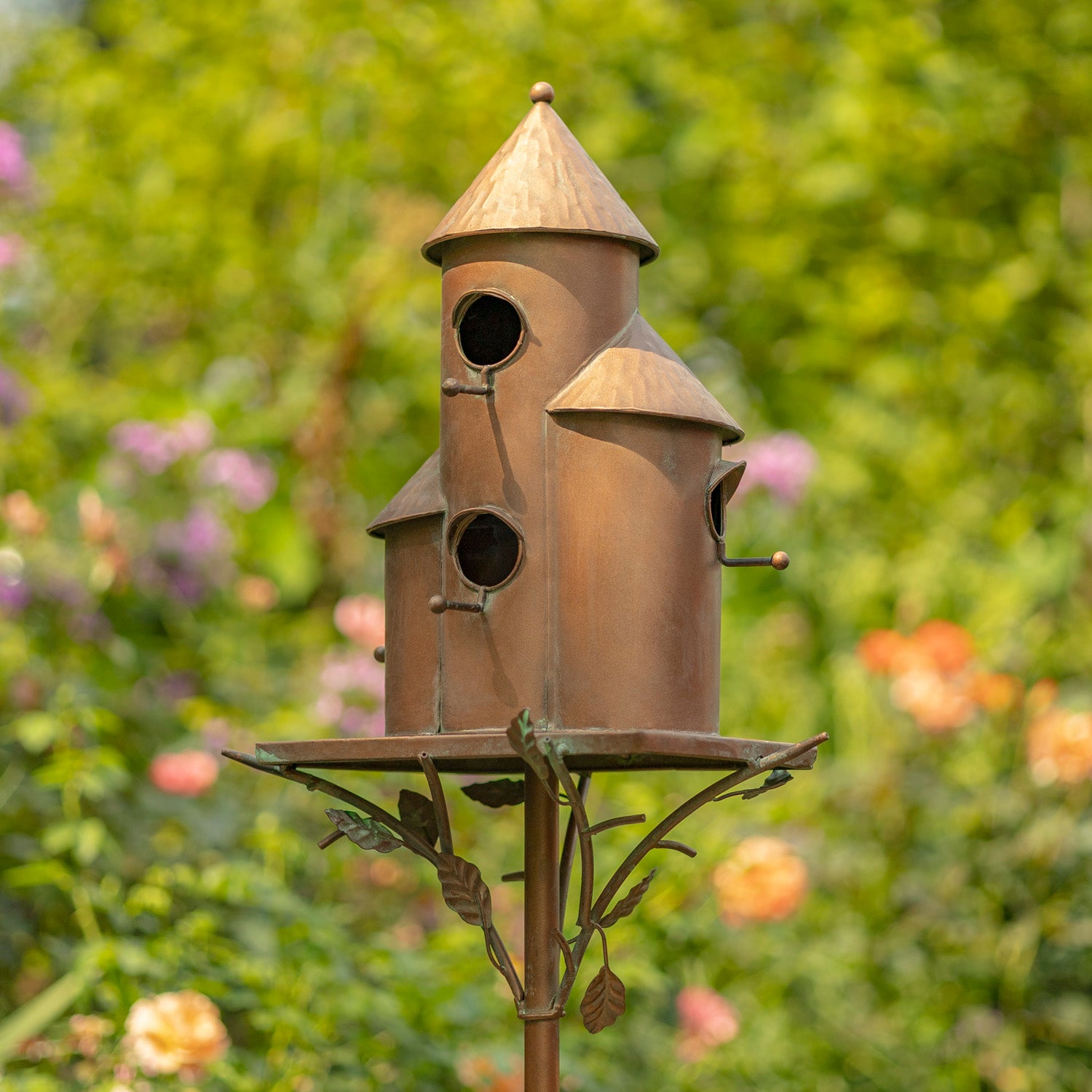 Decorative metal birdhouse on a stand with a garden background