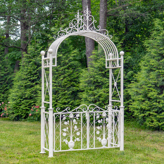 White metal garden arch with decorative top and bottom sections in a grassy area with trees.