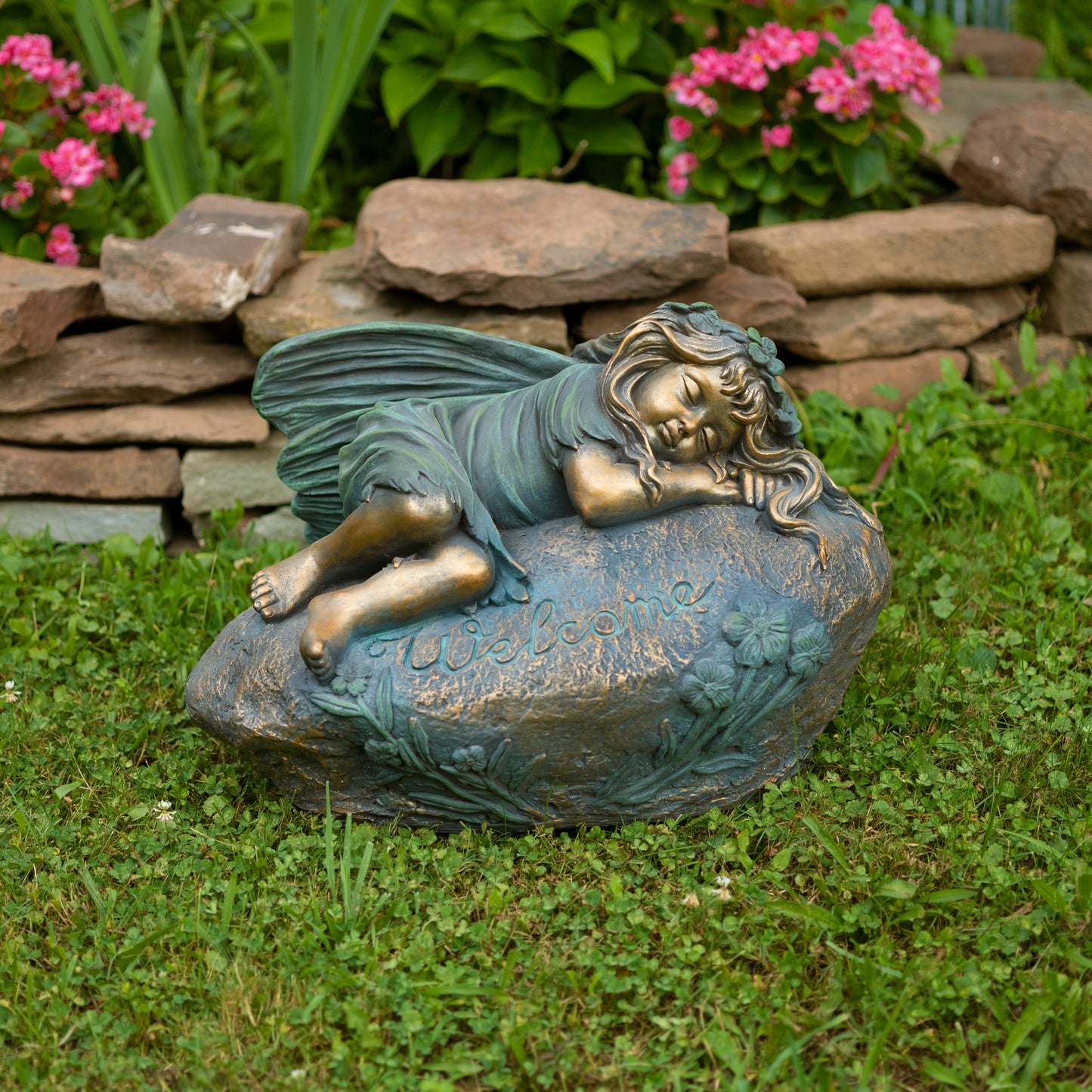 Garden statue of a fairy sitting on a rock with flowers and rocks in the background