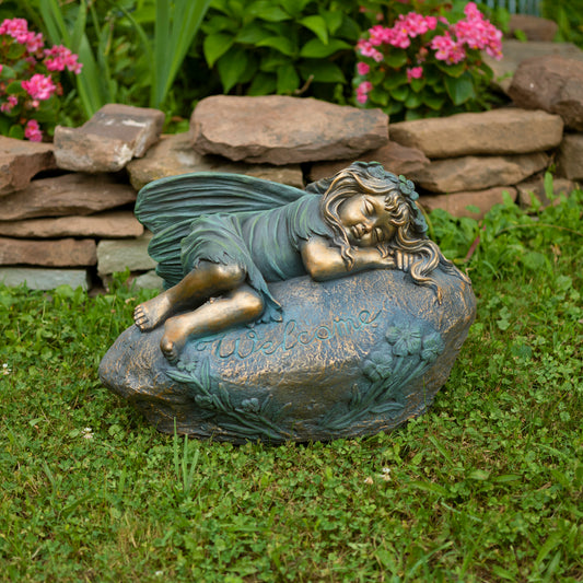 Garden statue of a fairy sitting on a rock with flowers and rocks in the background