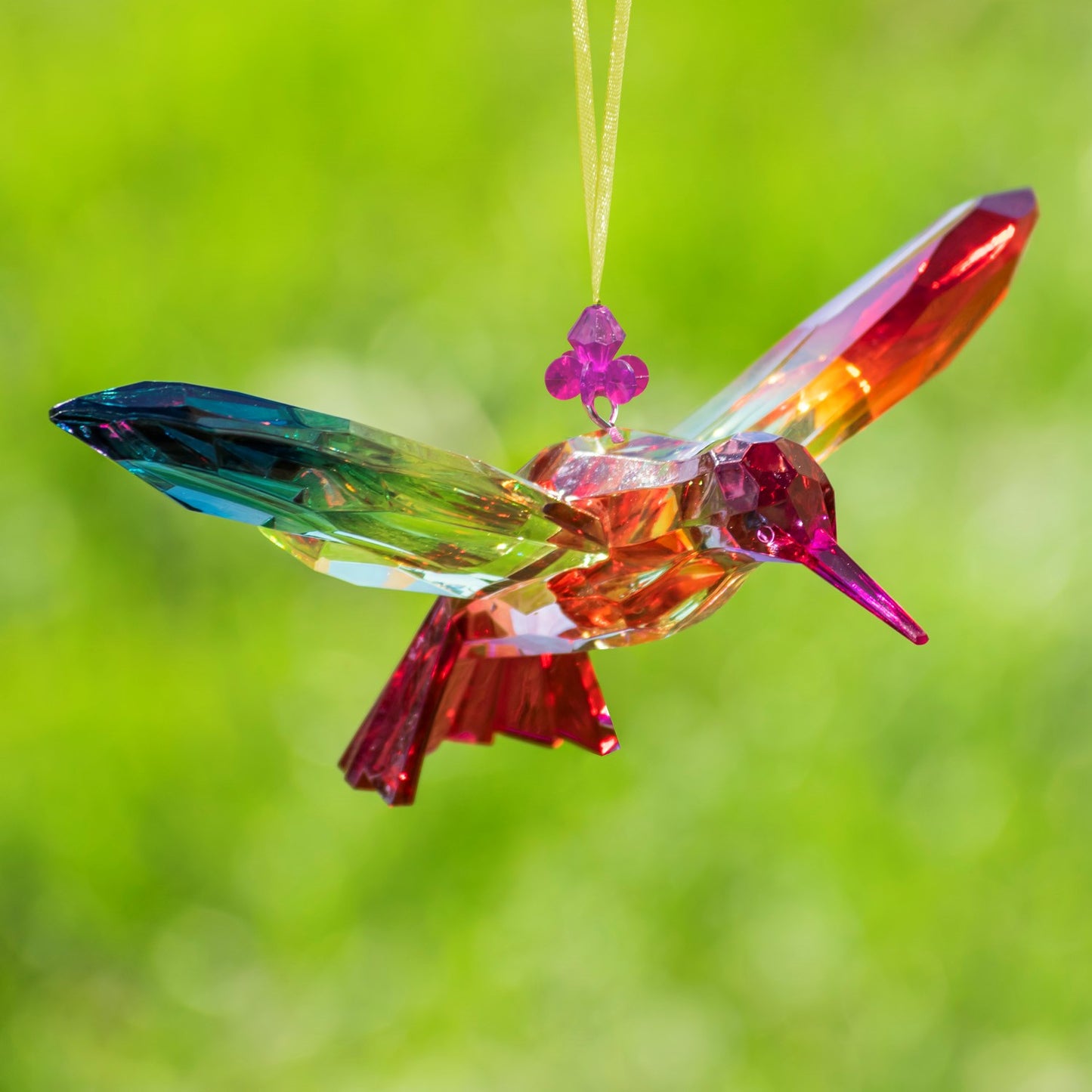 Colorful glass hummingbird ornament against a green background