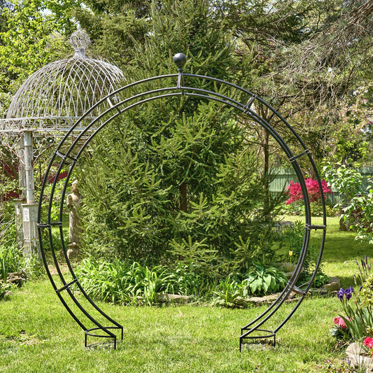 Circular metal garden archway in a lush garden setting with trees and flowers.
