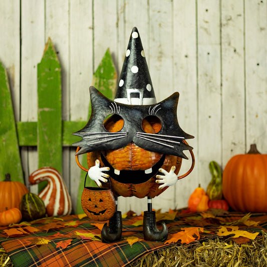 A Halloween decorative pumpkin figure wearing a black cat mask, pointed witch hat, and black boots, standing on a plaid blanket with autumn leaves and pumpkins around it.