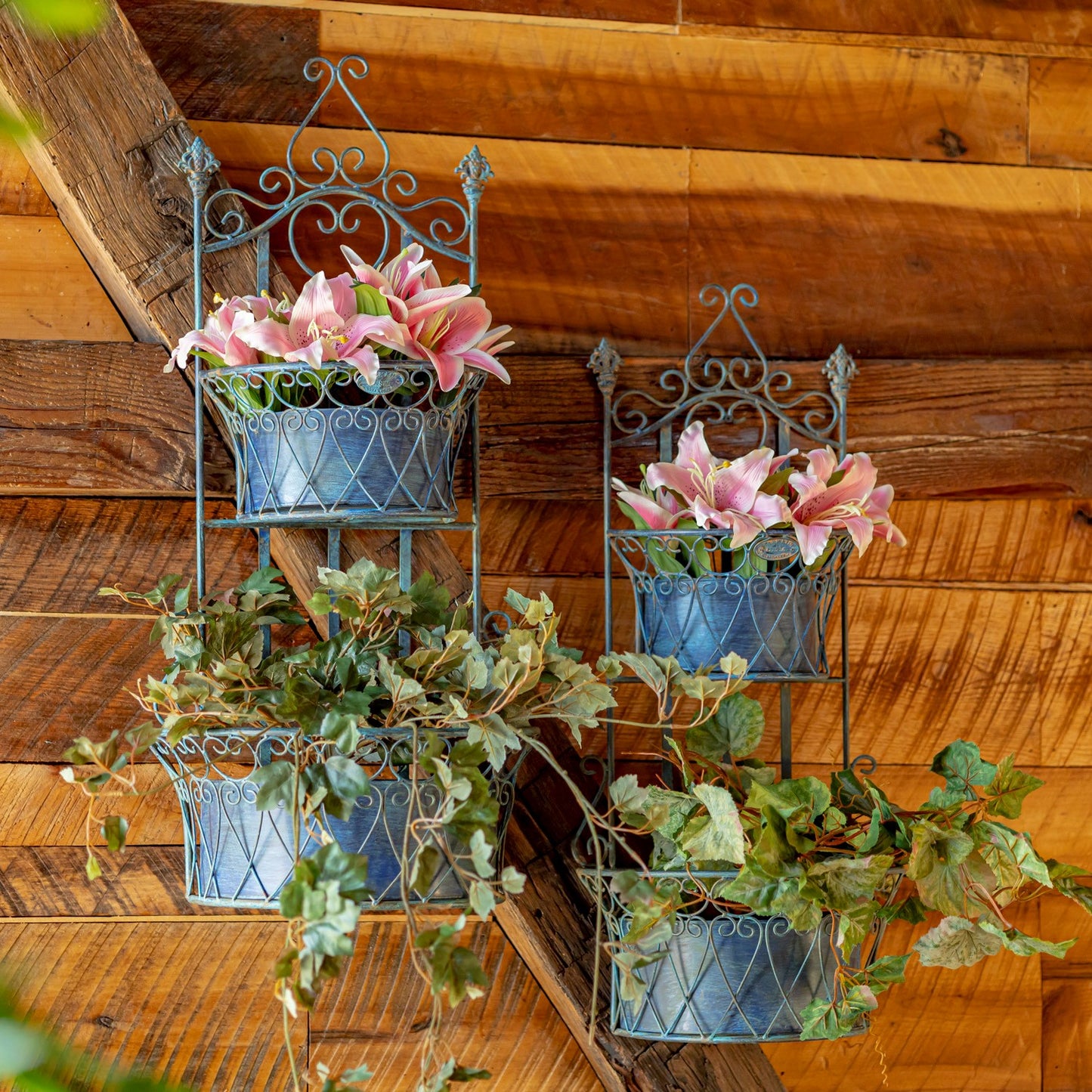 Wrought iron wall planters with flowers and greenery on a wooden wall.