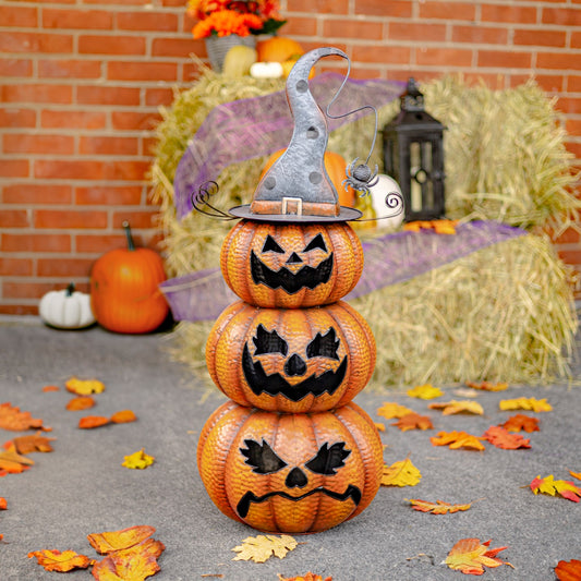 Stack of carved pumpkins with a witch hat on a Halloween-themed setting with hay bales and pumpkins.