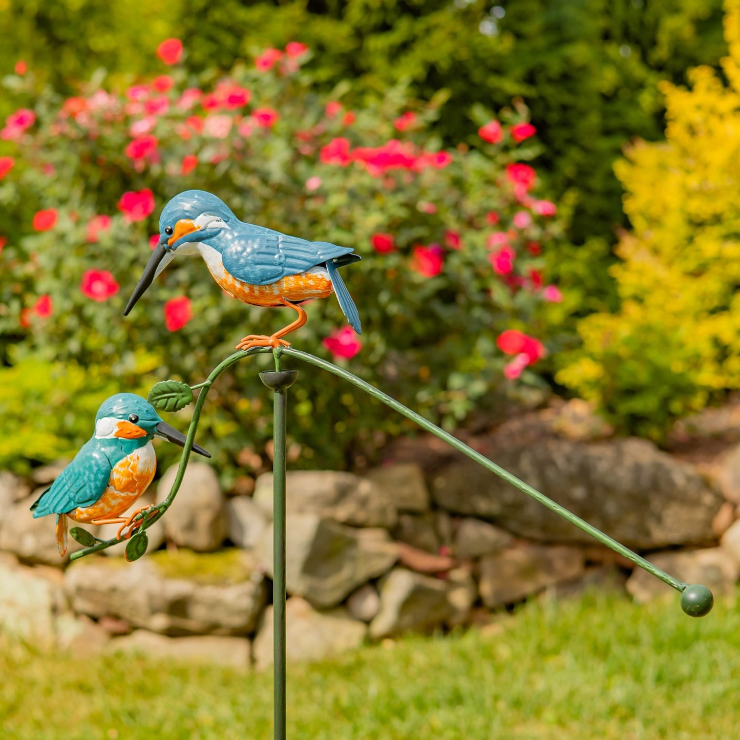 Decorative garden stake with two blue and orange bird figures against a garden backdrop.