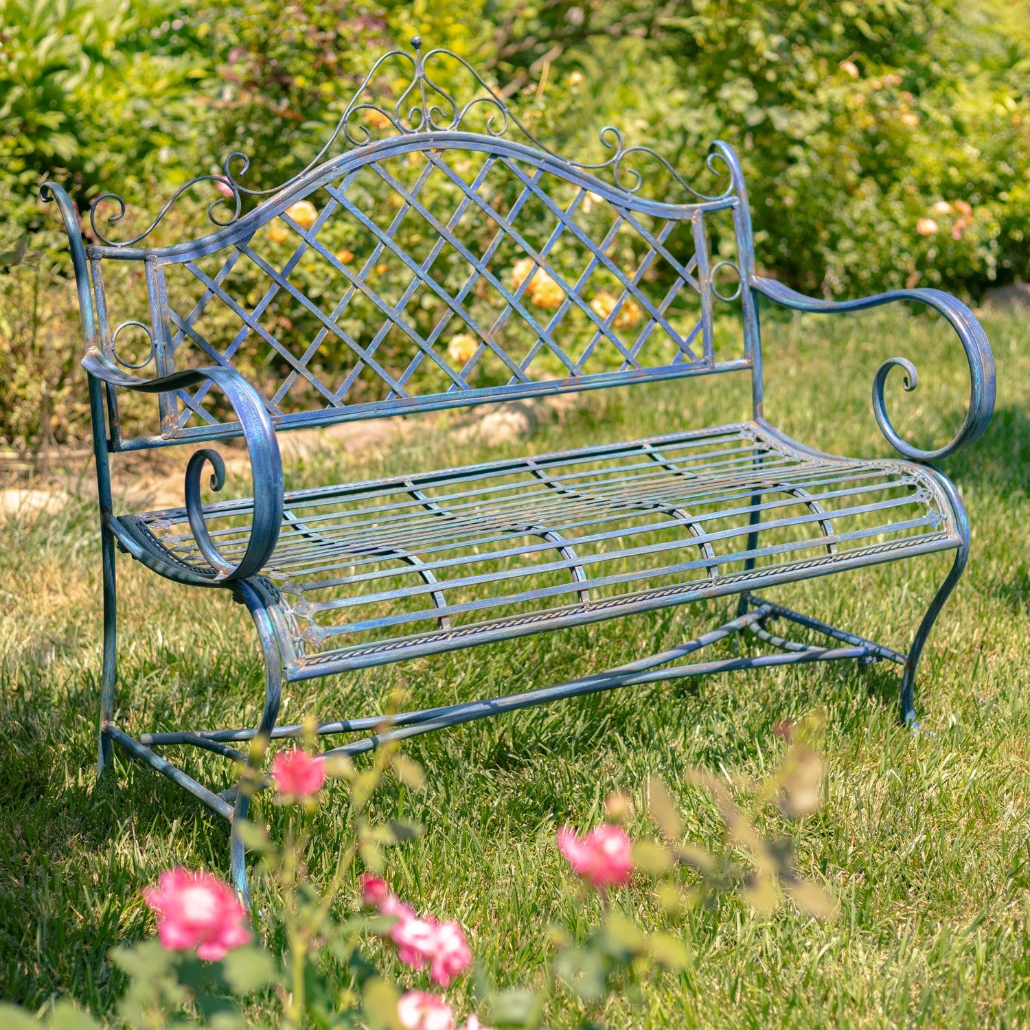 Decorative metal garden bench in a grassy area with flowers