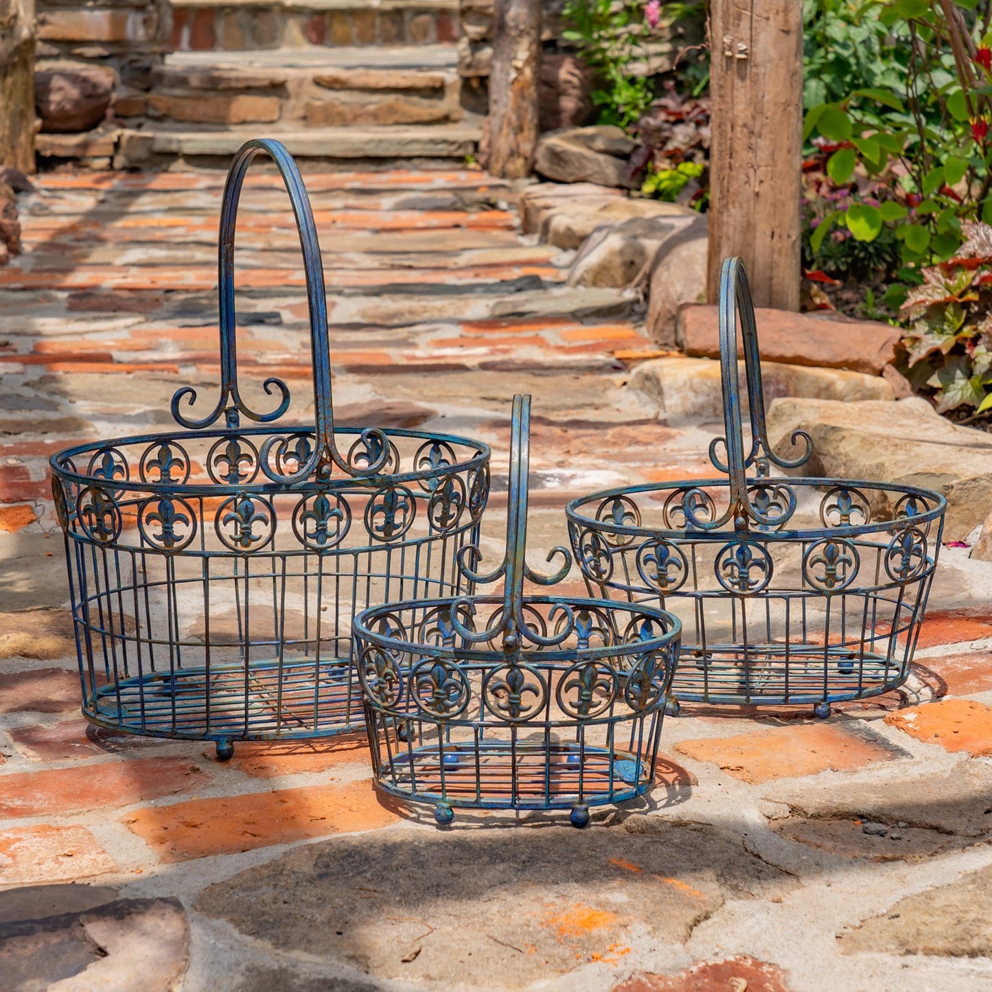 Three dark blue metal wire baskets with decorative scrollwork and arched handles, arranged on a stone patio outdoors.
