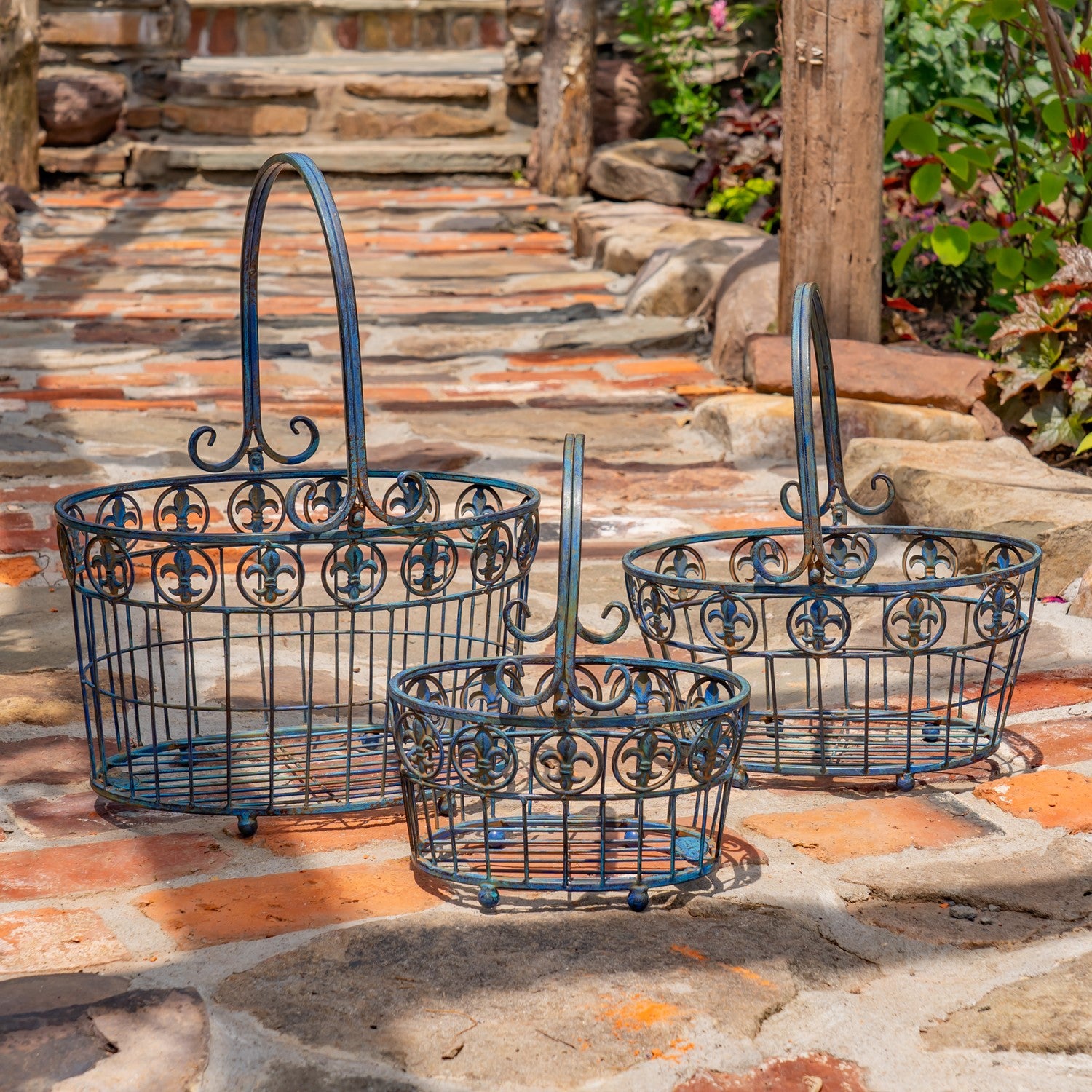 Three dark blue metal wire baskets with decorative scrollwork and arched handles, arranged on a stone patio outdoors.