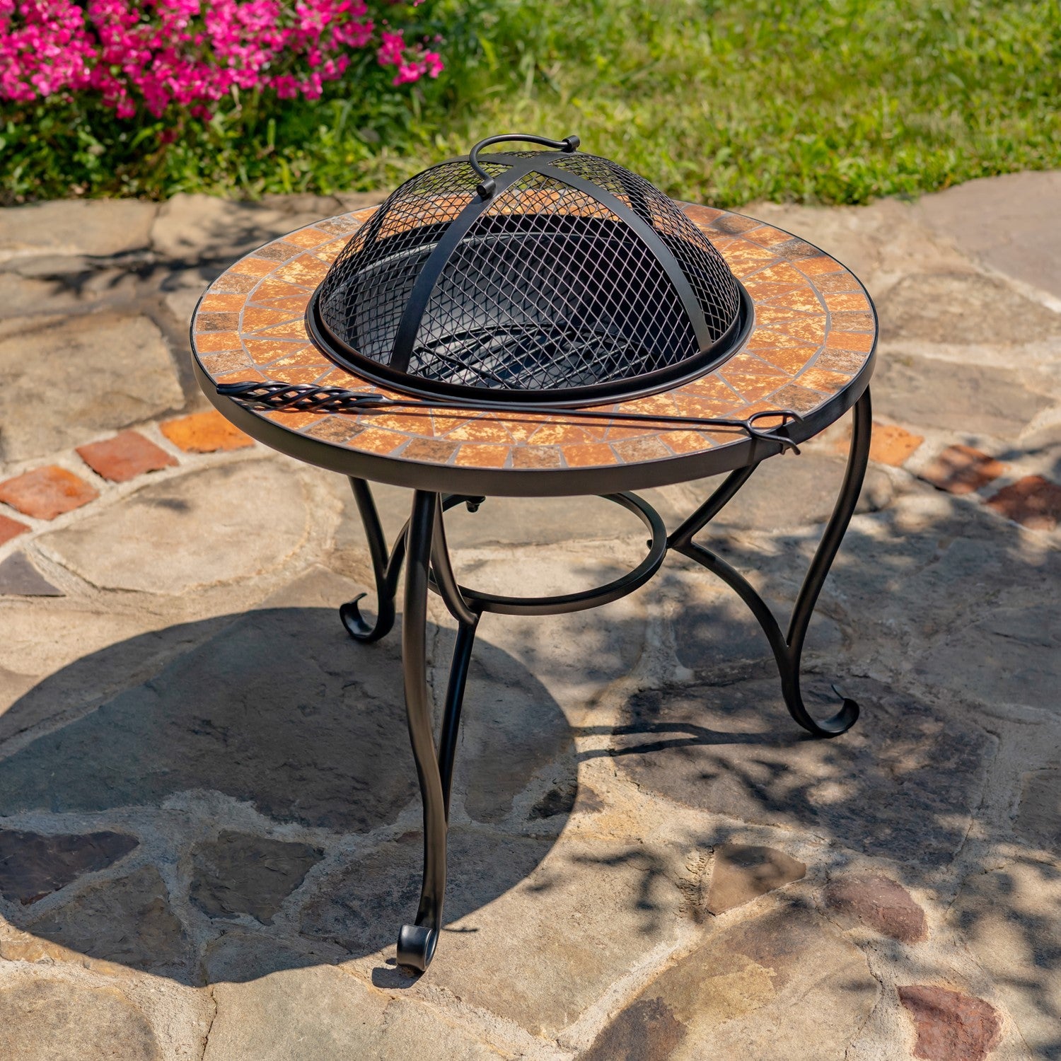 Outdoor fire pit table with decorative mosaic top on a stone patio