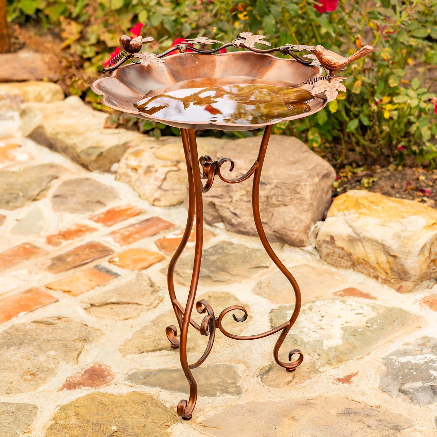 Flower shaped birdbath with ivy and birds sitting on the side in a garden setting