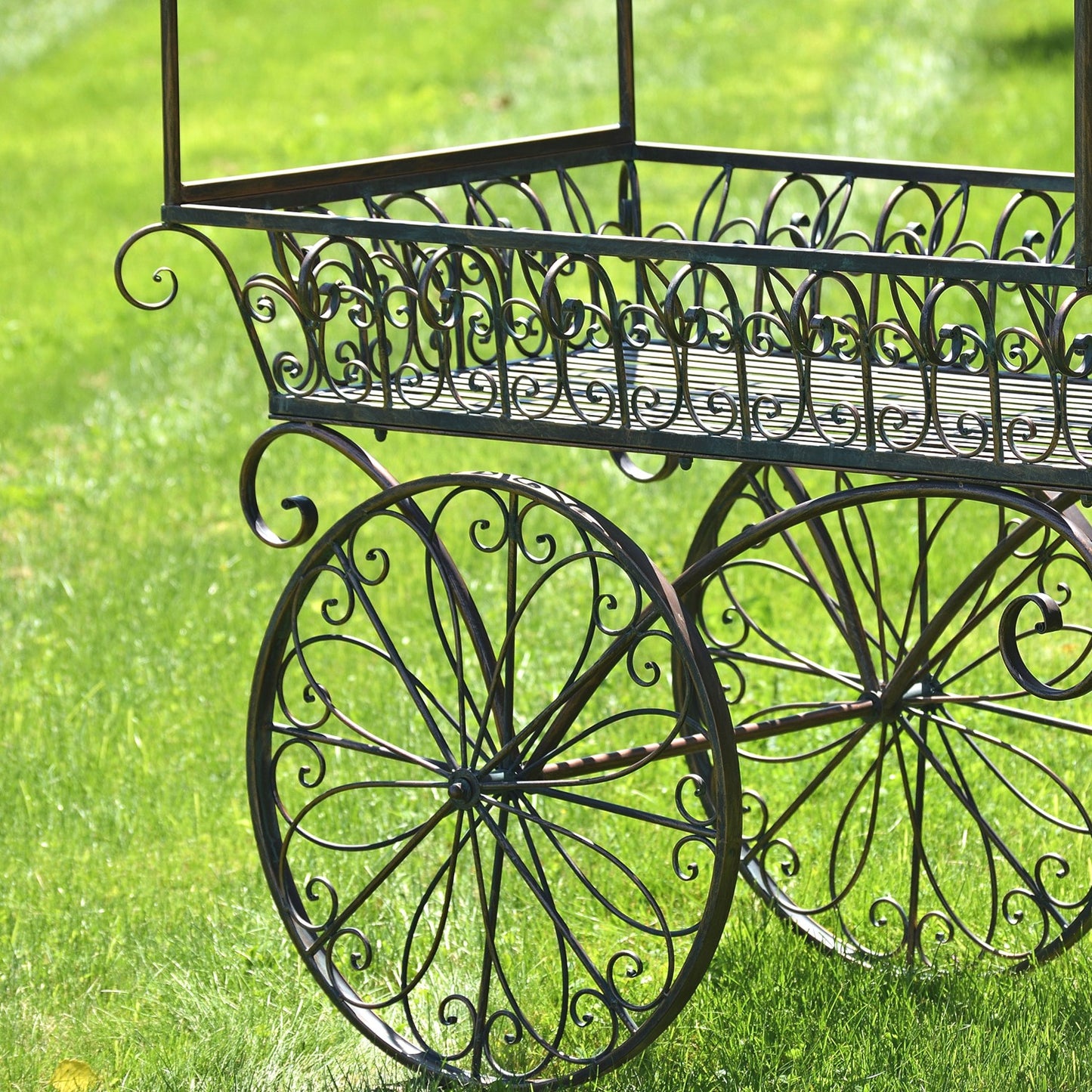 Black wrought iron decorative cart with ornate scrollwork and large spoked wheels, photographed outdoors on green grass.