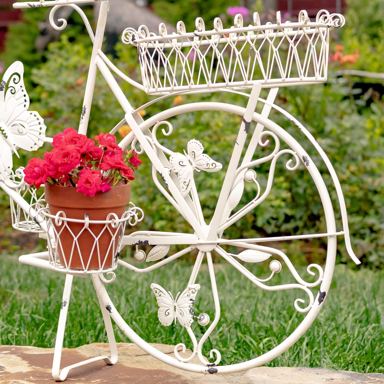 Decorative white metal bike sculpture with flower pots and butterfly details in a garden setting