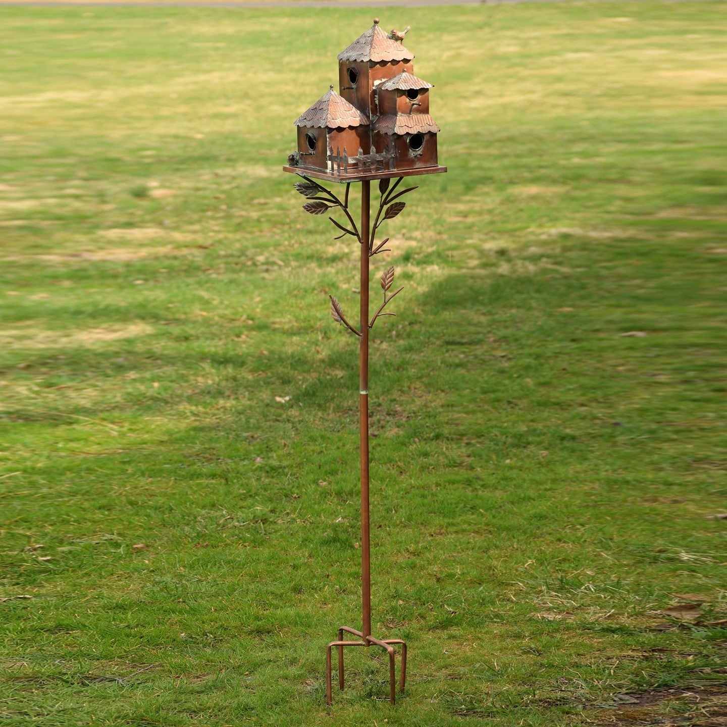 A rustic metal windmill garden ornament mounted on a tall pole, set against a green grassy field.