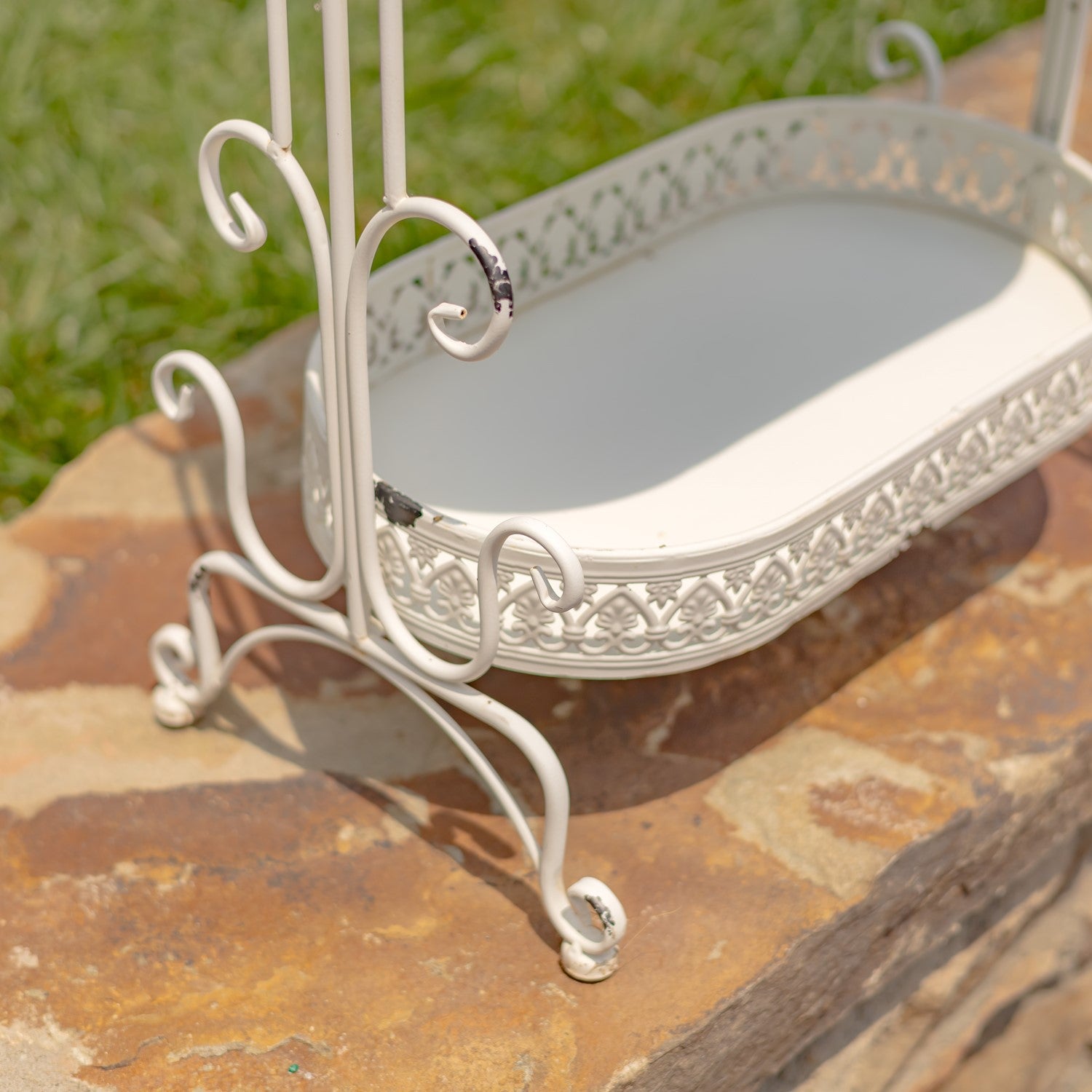Decorative white metal stand with an oval tray on a stone surface