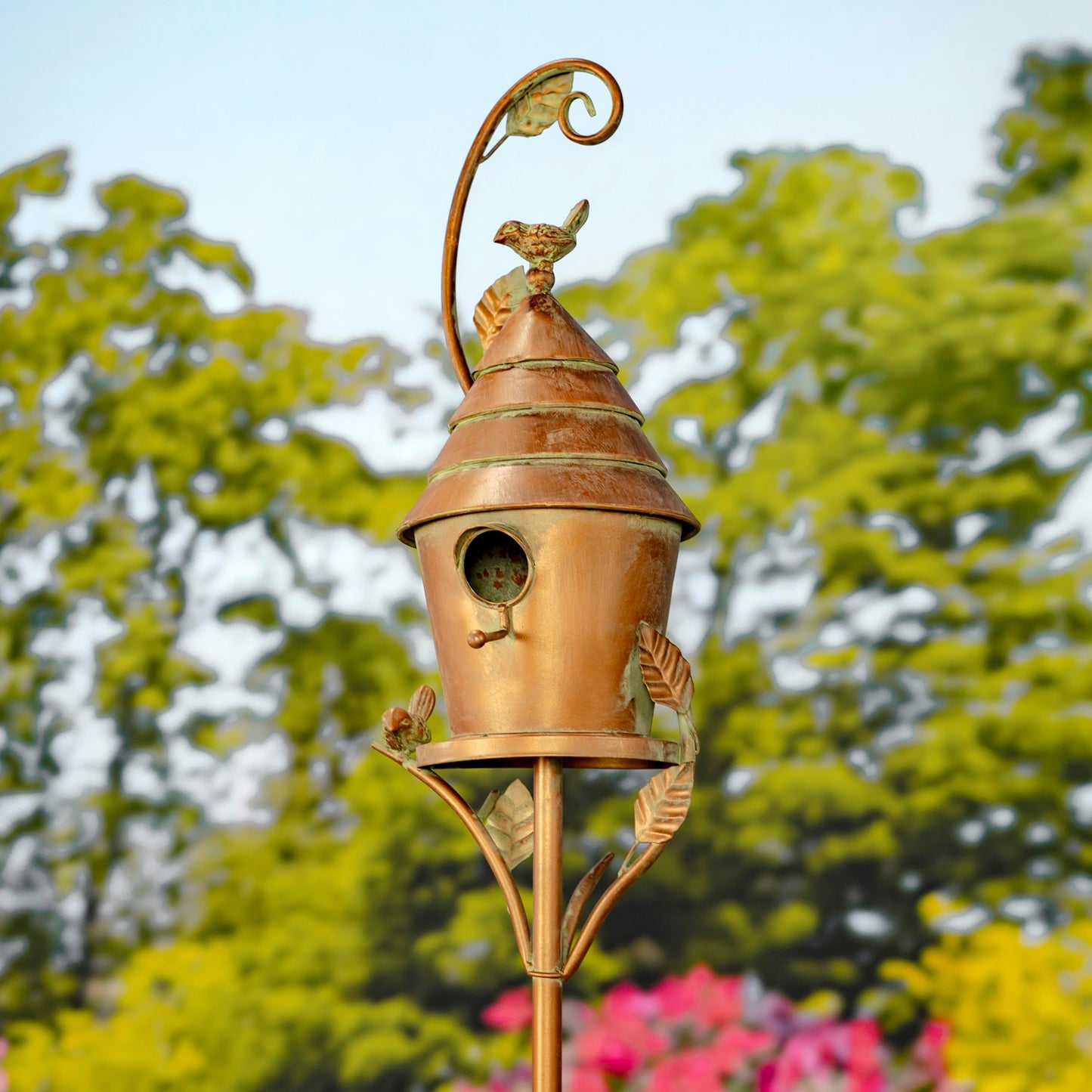 Decorative copper birdhouse on a stand with a blurred garden background