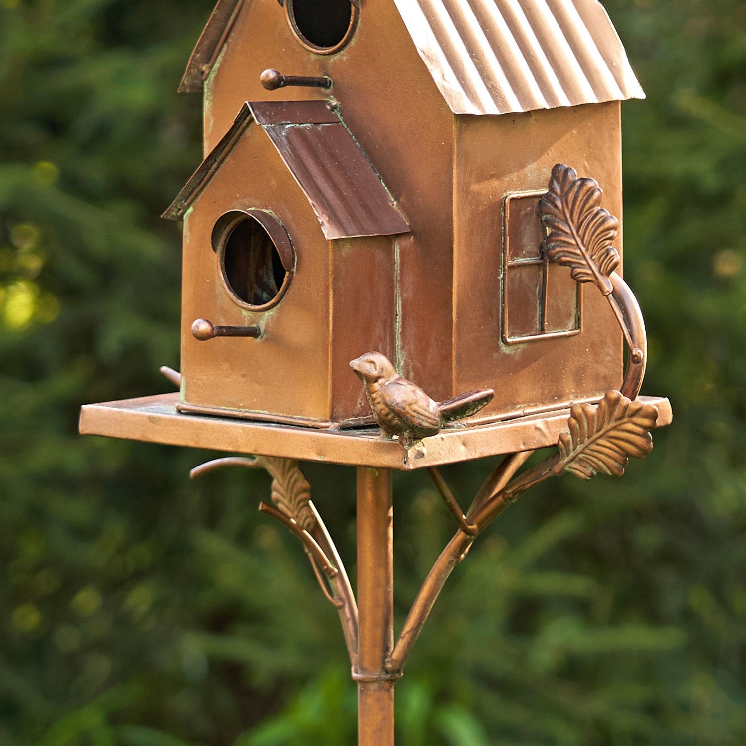 Decorative copper birdhouse with a bird on a stand against a blurred green background