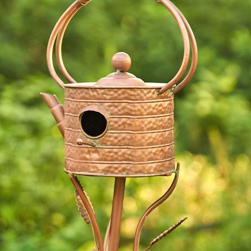 Copper birdhouse with a decorative stand against a blurred green background
