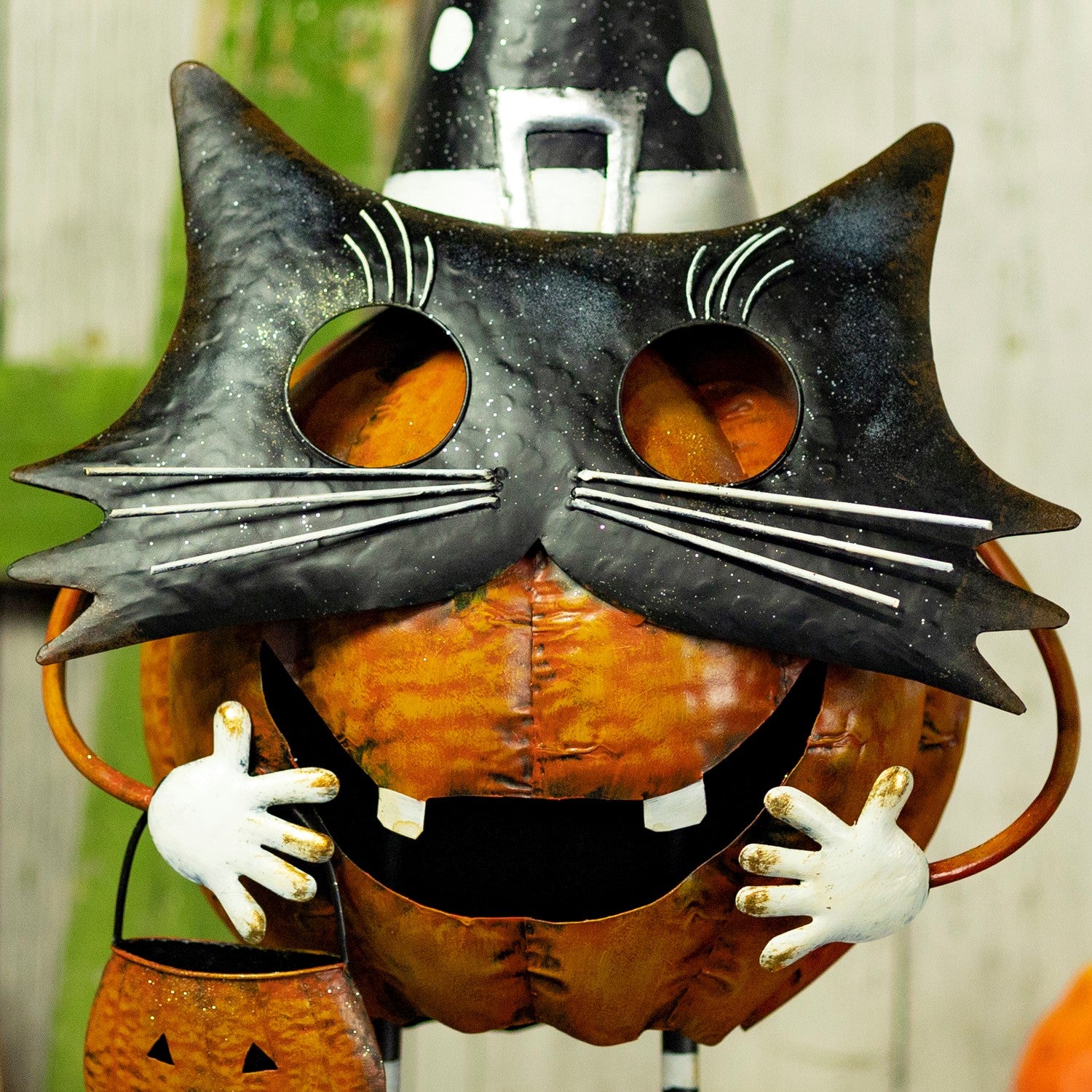 A Halloween decorative pumpkin sculpture with a black cat face mask, orange pumpkin body, white hands, and a small orange pumpkin bucket.