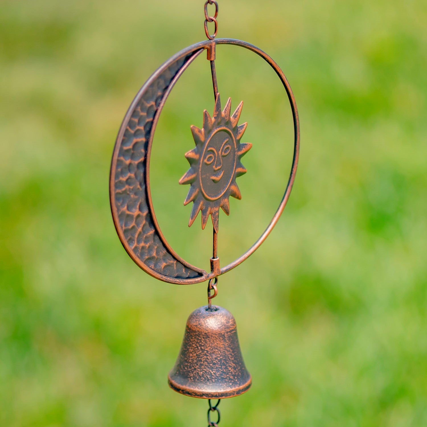 Decorative copper wind chime with sun and moon design against a blurred green background