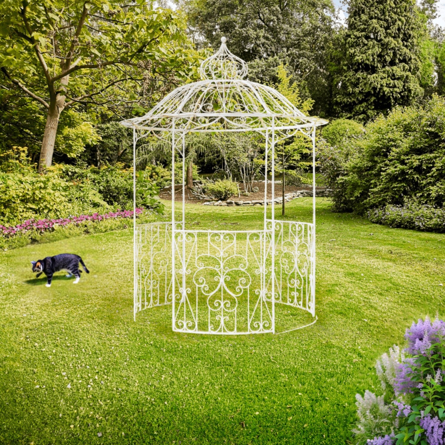 A white wrought-iron garden gazebo with an ornate openwork design stands on a green lawn in a landscaped garden. A black dog is visible on the left side of the lawn, and purple flowers appear in the lower right corner.