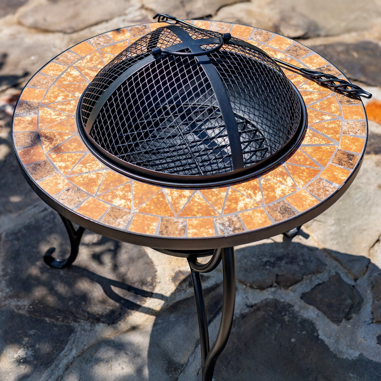 Round stone-patterned fire pit table with black metal fire basket on a stone patio.