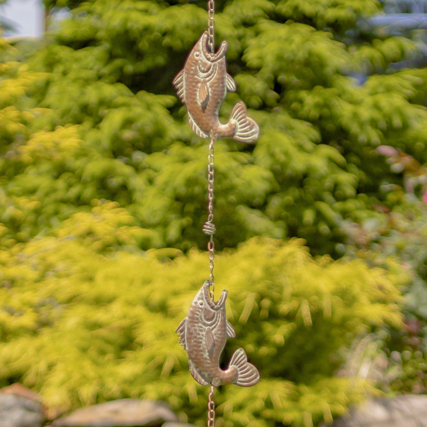 Decorative fish-shaped wind chime hanging against a green bush background