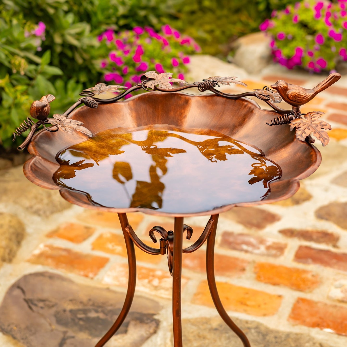 Flower shaped birdbath with ivy and birds sitting on the side in a garden setting