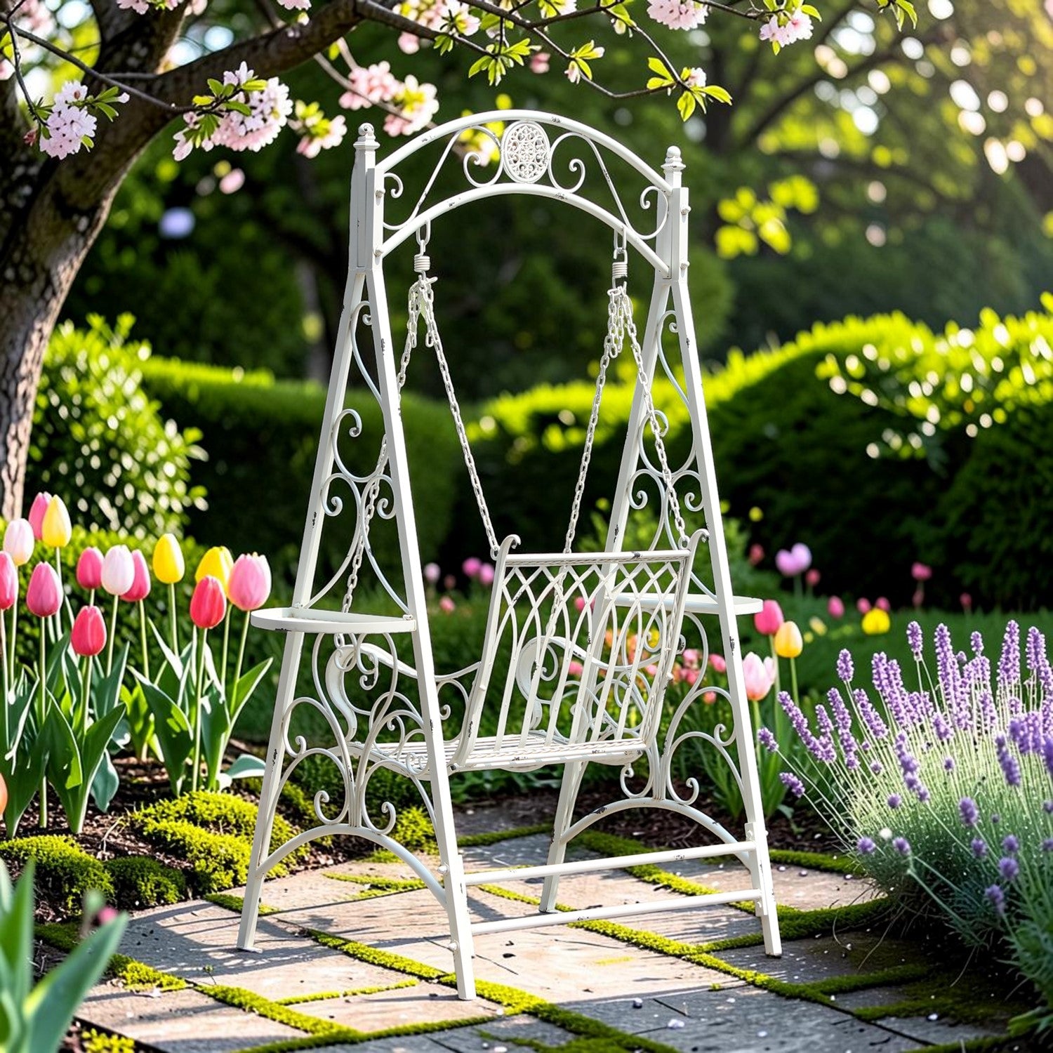 A white wrought-iron garden swing bench with decorative scrollwork, set on a stone path in a lush garden with pink tulips and lavender.