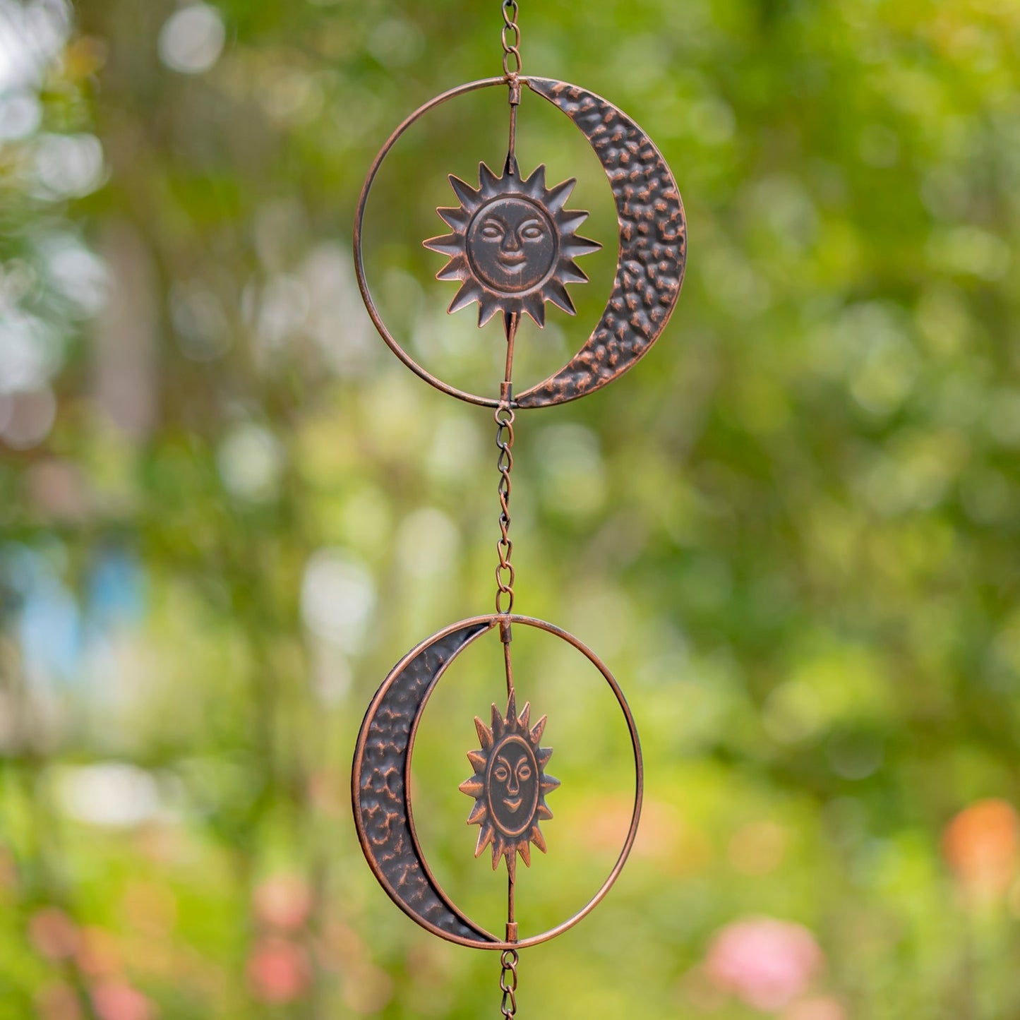 Decorative metal hanging with sun and moon designs against a blurred green background