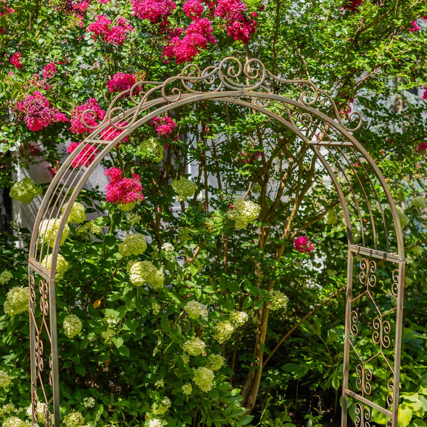Decorative metal archway in a garden with pink and green flowers
