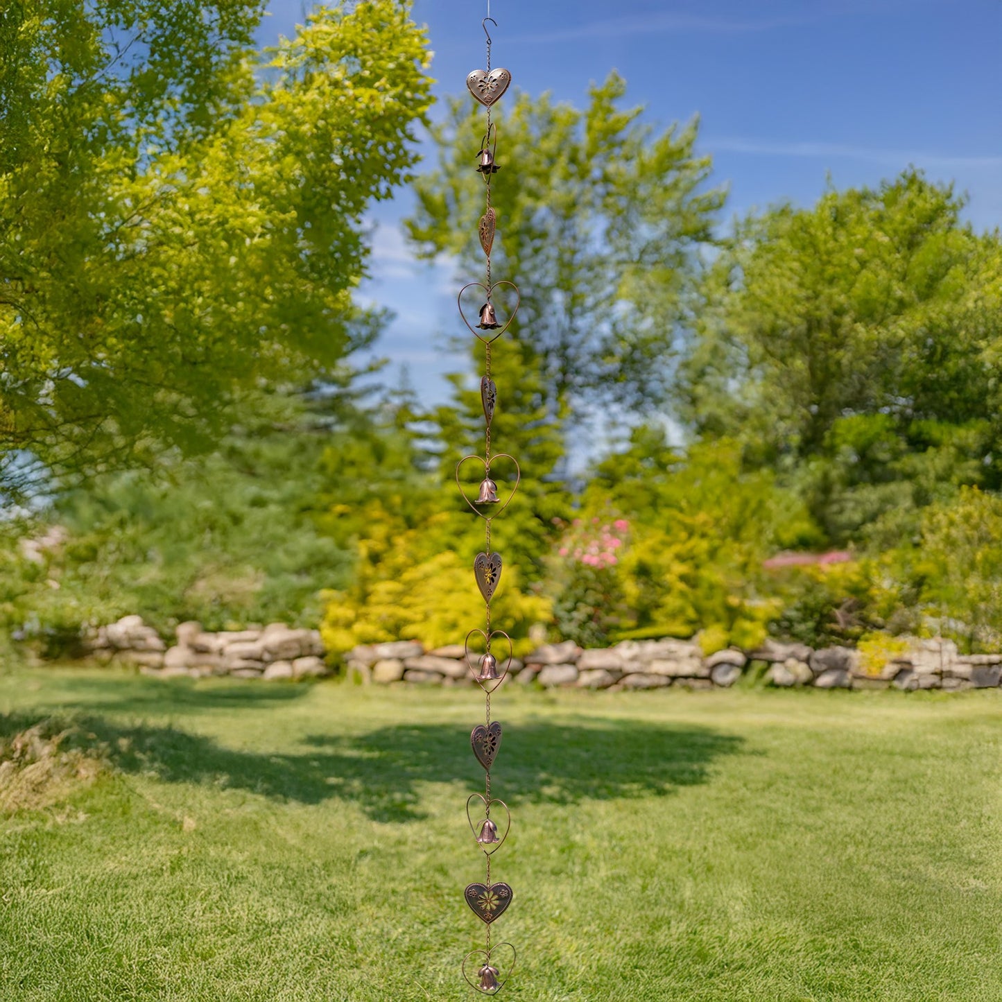 A copper-toned metal garden wind spinner featuring a bell-shaped flower suspended inside a heart-shaped wire frame, set against a blurred green grass background.