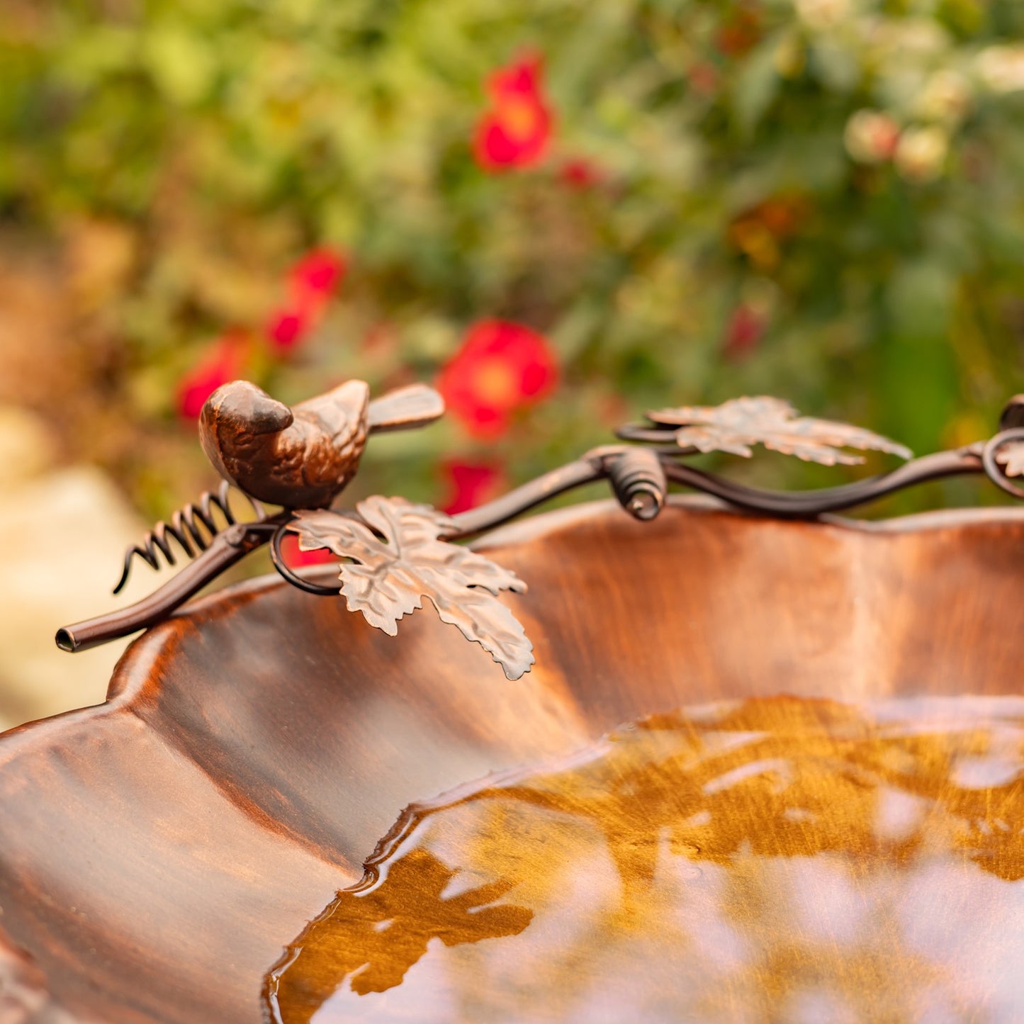 Flower shaped birdbath with ivy and birds sitting on the side in a garden setting
