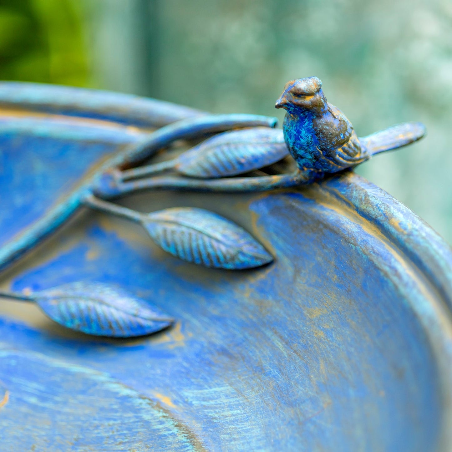 Decorative blue bird figurine on a metallic surface with a blurred green background