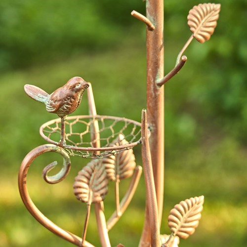 Decorative metal bird on a branch with leaves against a blurred green background