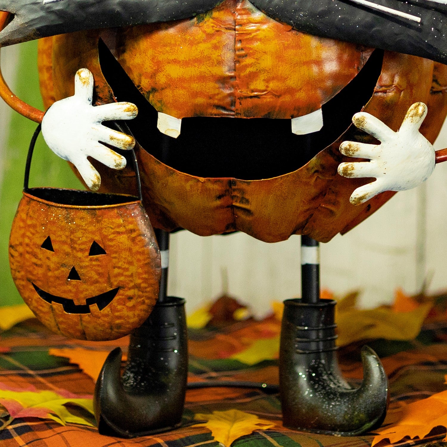 A Halloween pumpkin decoration shaped like a stitched orange jack-o'-lantern with a black hat, white hands, and black boots, holding a small matching pumpkin bucket.