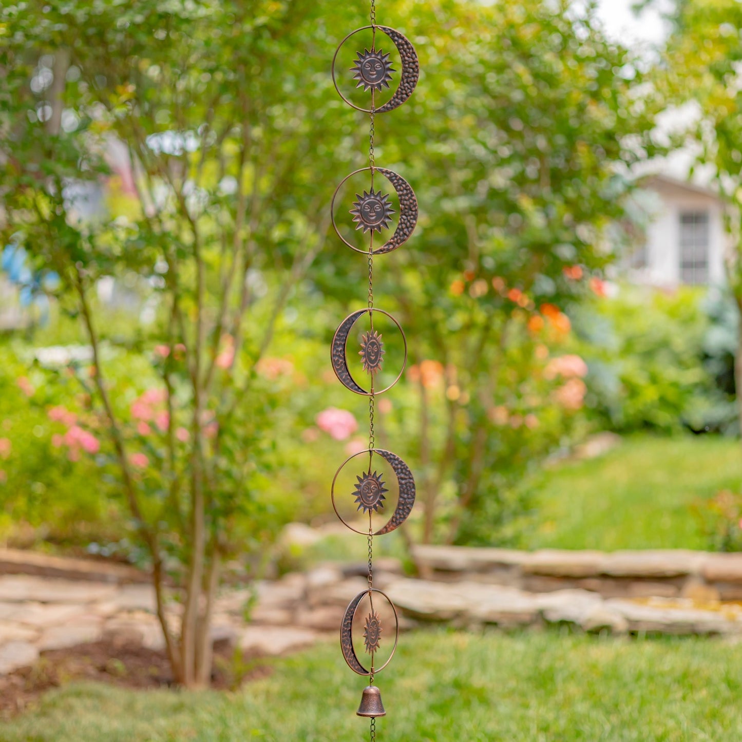 Decorative metal wind chime with celestial designs hanging in a garden.