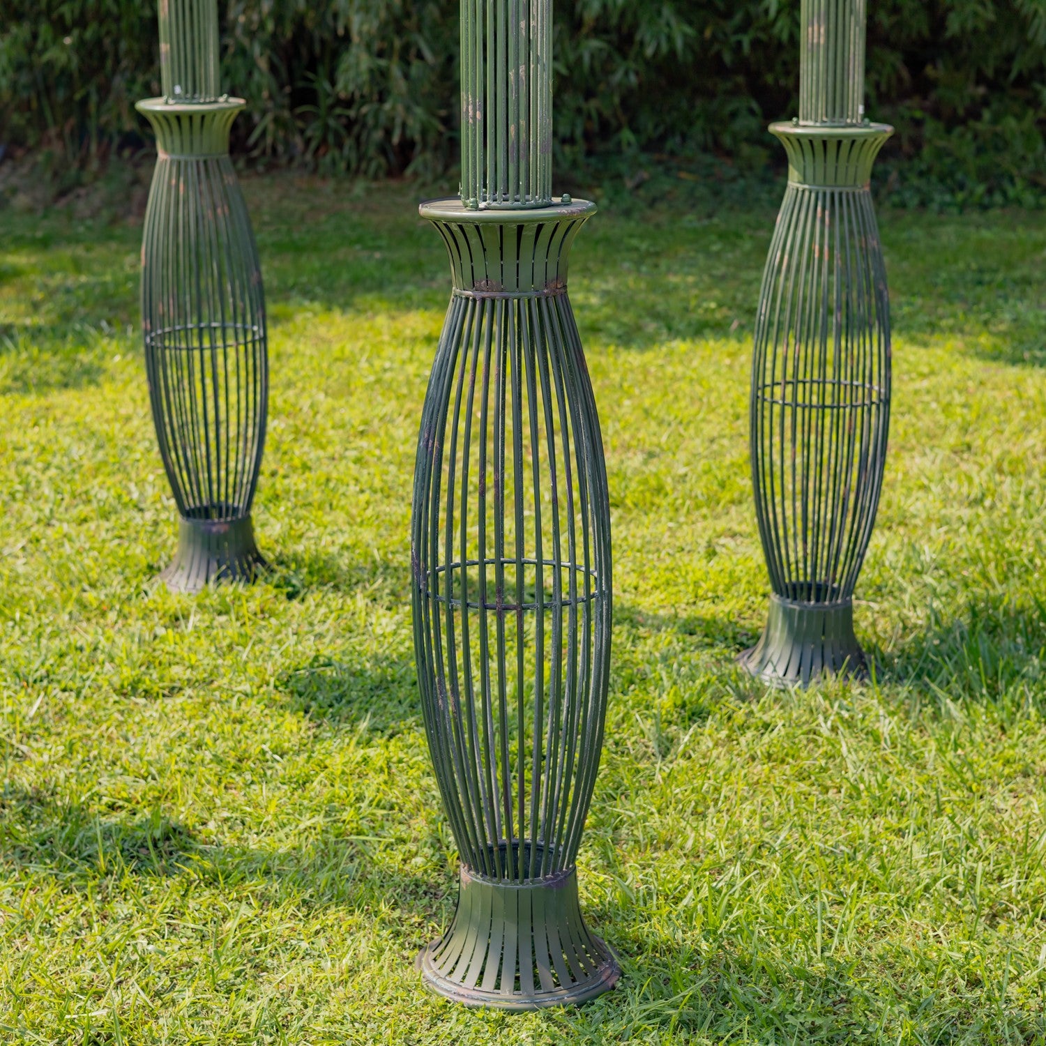 Three dark metal garden column guards with a ribbed, vase-like design standing on a green grass lawn.