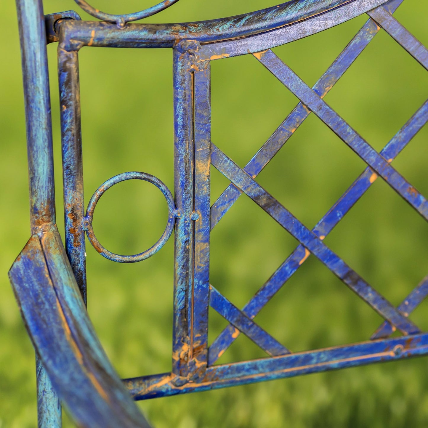 Close-up of a blue metal garden chair with a distressed, rusted finish and a lattice backrest, set against a blurred green grass background.